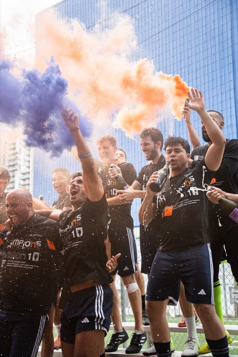 Champions spraying champagne under orange smoke after winning the Corporate Fútbol League